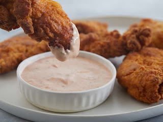 chicken dipping into the bowl of Sauce with another chicken piece in background