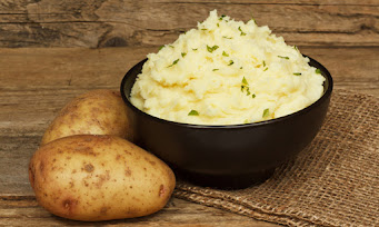 A bowl with mashed potatoes in it and 2 whole potatoes on side